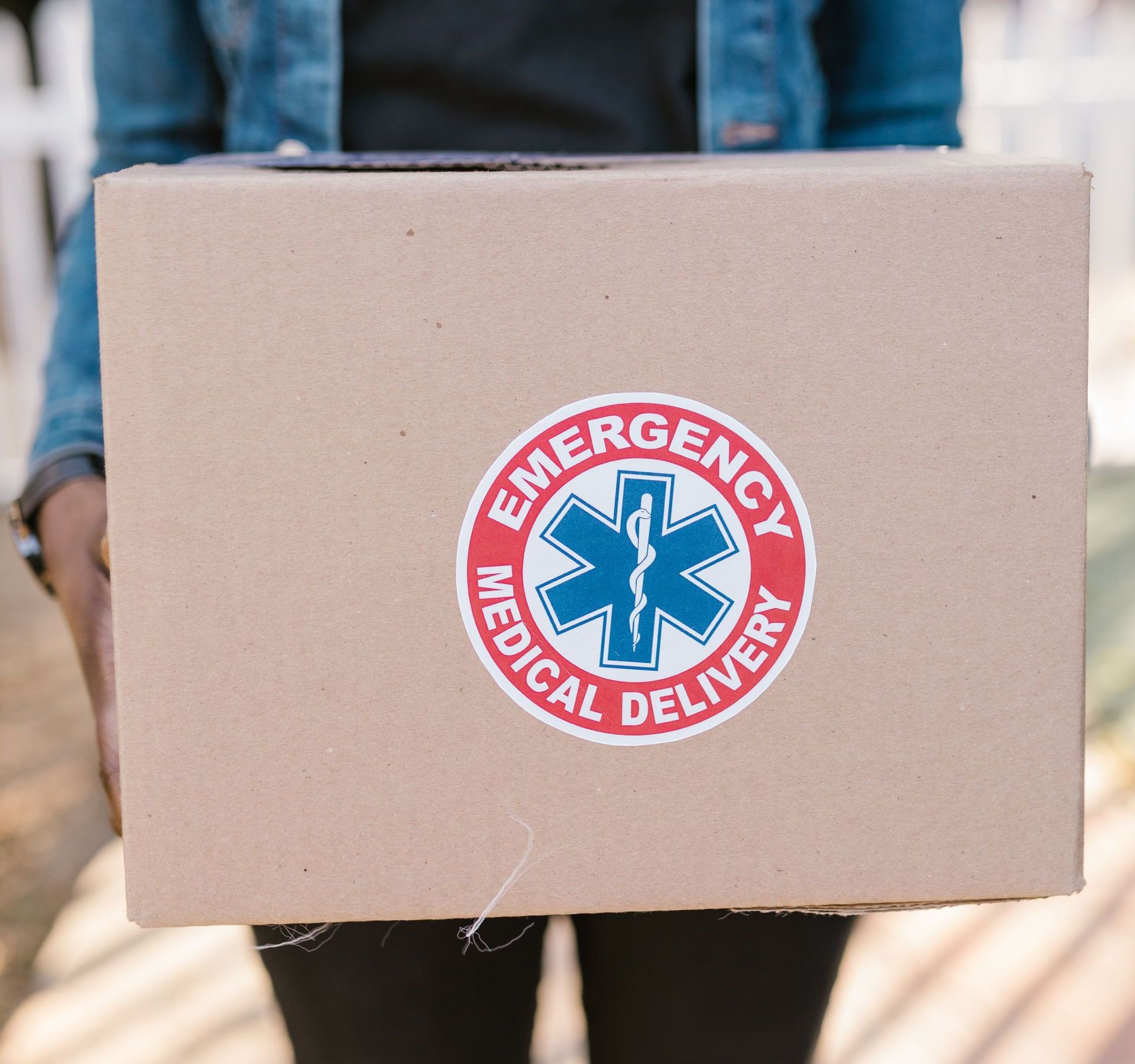 Person holding a box labeled 'Emergency Medical Delivery,' representing urgent healthcare logistics.